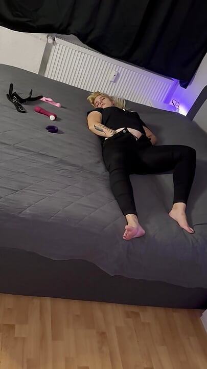 Blonde lady in black gets orgasms while standing behind the camera and watching her