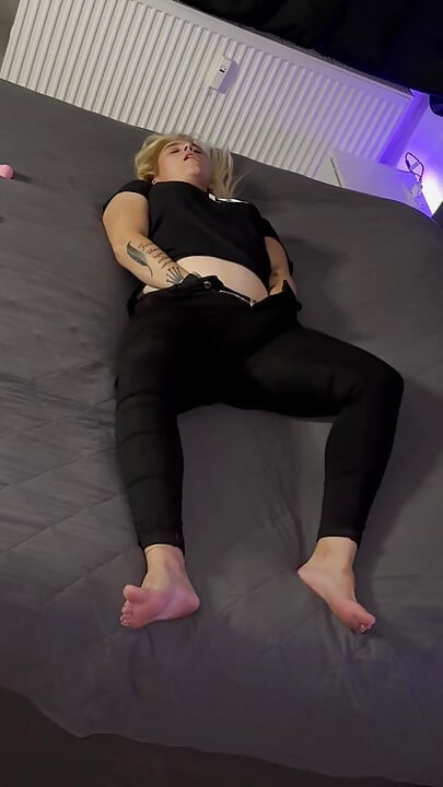 Blonde lady in black gets orgasms while standing behind the camera and watching her