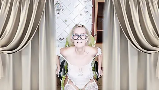Cheerful housewife Lukerya flirts in an open, transparent white jumpsuit in the kitchen.