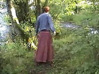 Rijpe exhibitionistische vrouw speelt met zichzelf bij de rivier