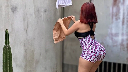 Mucama con gran trasero con ropa sexy colgando ropa en el tendedero en el patio trasero