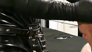 Un maître dominant en latex avec son adorateur de bottes en cage