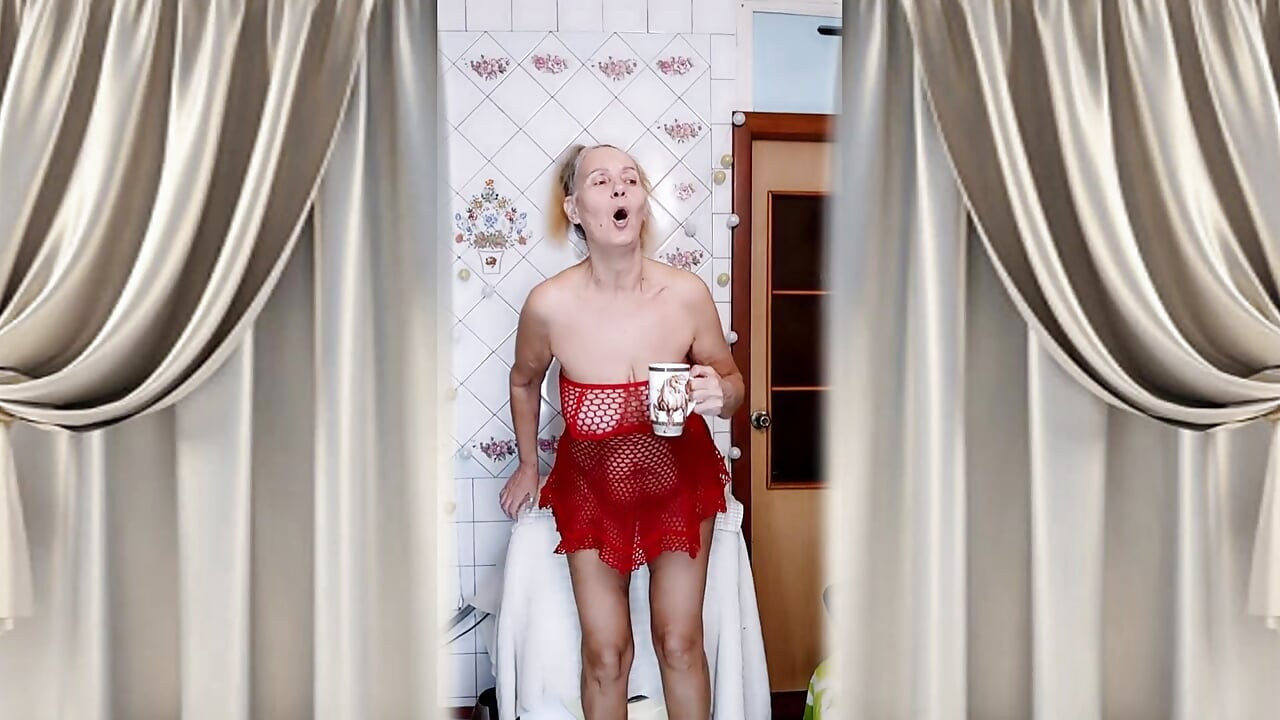 Heiße hausfrau Lukerya flirtet über den morgen kaffee in einem roten netzkleid.