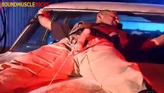 Agent Derek da Silva vastgebonden aan de motorkap van een auto