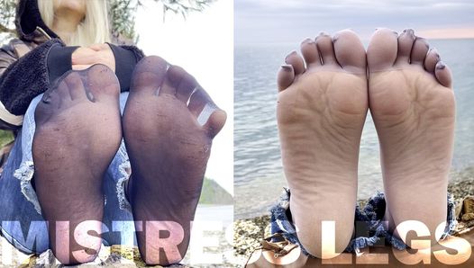 海岸で足を揺らす黒とグレーのナイロン靴下の足