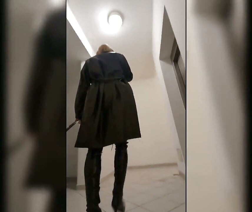 Caminhada na casa de estacionamento, loira em botas overknee, vestido vermelho de pvc e casaco de couro longo