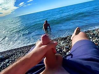 Un mec branle une bite sur une plage nudiste et un passant l’a rejoint