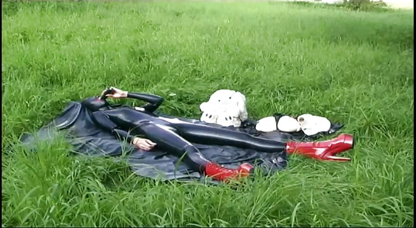 Esclavo fetiche en látex camina y chupa un consolador en la hierba