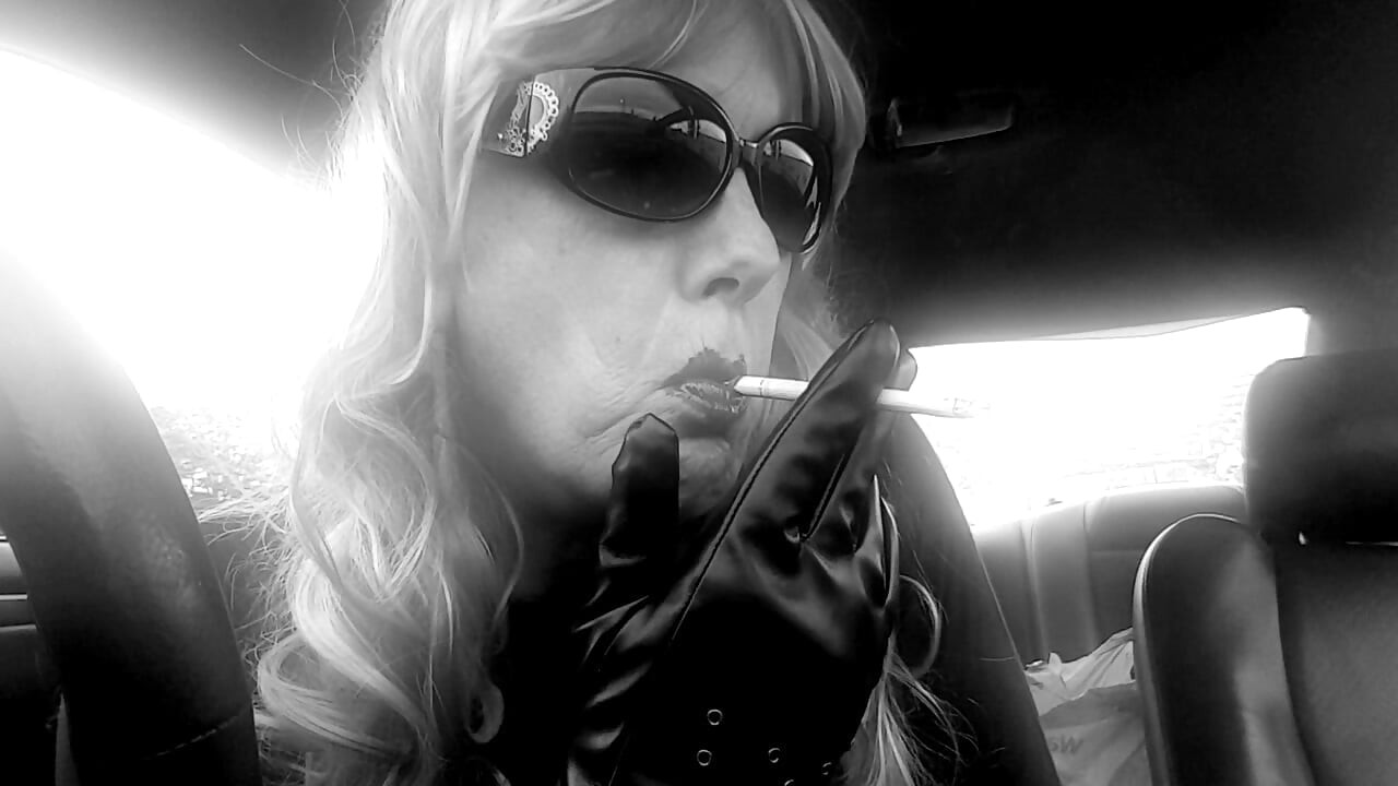 Зряла TG CD с перука с дъга и кожени ръкавици пуши VS120s като професионалистка в колата си