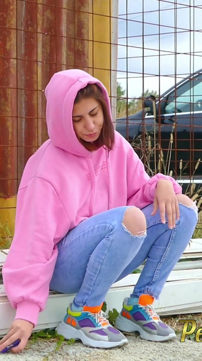 Hipster girl with a hoodie pee trough her jeans and pee next to the wheel of the car