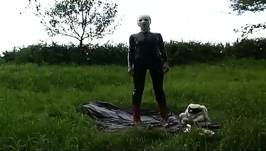 Fetish slave in latex walks and sucks a dildo on the grass