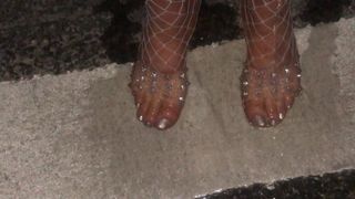 Al aire libre en medias de red y sandalias transparentes meando en los pies