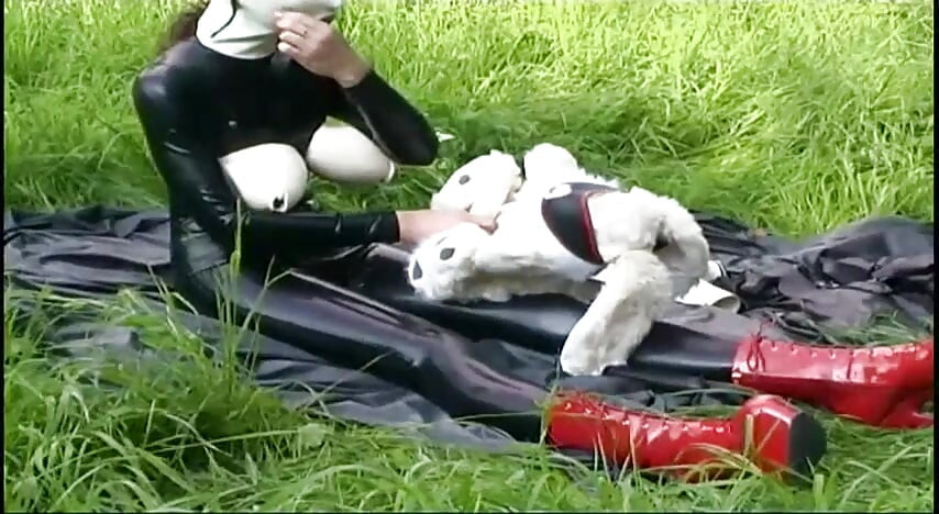 Fetish slave in latex walks and sucks a dildo on the grass