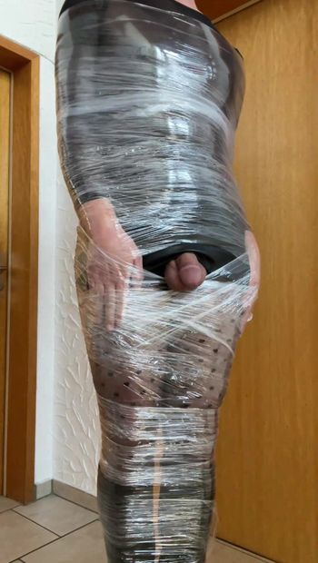 Travesti habillé de bottes en cuir en collants et jupe moulante enveloppée de papier plastique, momification, auto-bondage