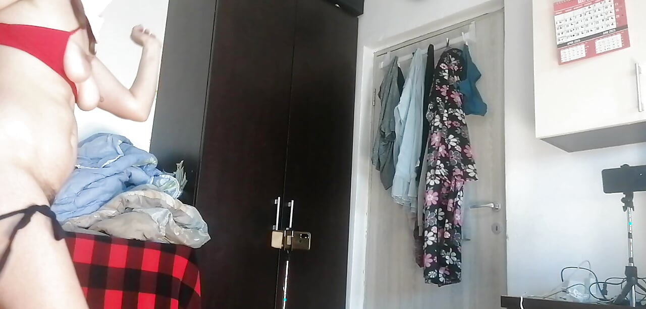 Amaterska žena pleše gola kod kuće. Amaterska žena se zabavlja isprobavajući odjeću i šišajući je.