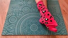 Gloria Gimson in calzini rosa si accarezza i piedi su un tappetino da yoga