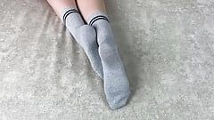 La ragazza a letto accarezza le gambe in calzini di cotone grigio