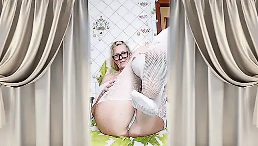 Cheerful housewife Lukerya flirts in an open, transparent white jumpsuit in the kitchen.