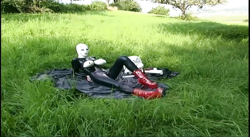 Fetischslav i latex går och suger en dildo på gräset
