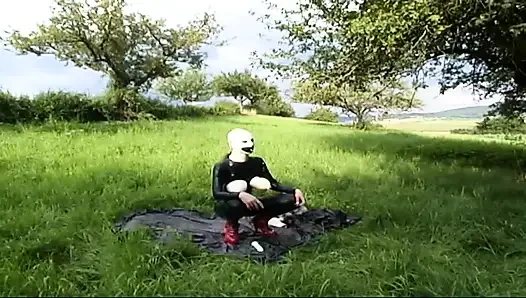 Fetisch-sklavin in latex geht und lutscht einen dildo auf dem gras