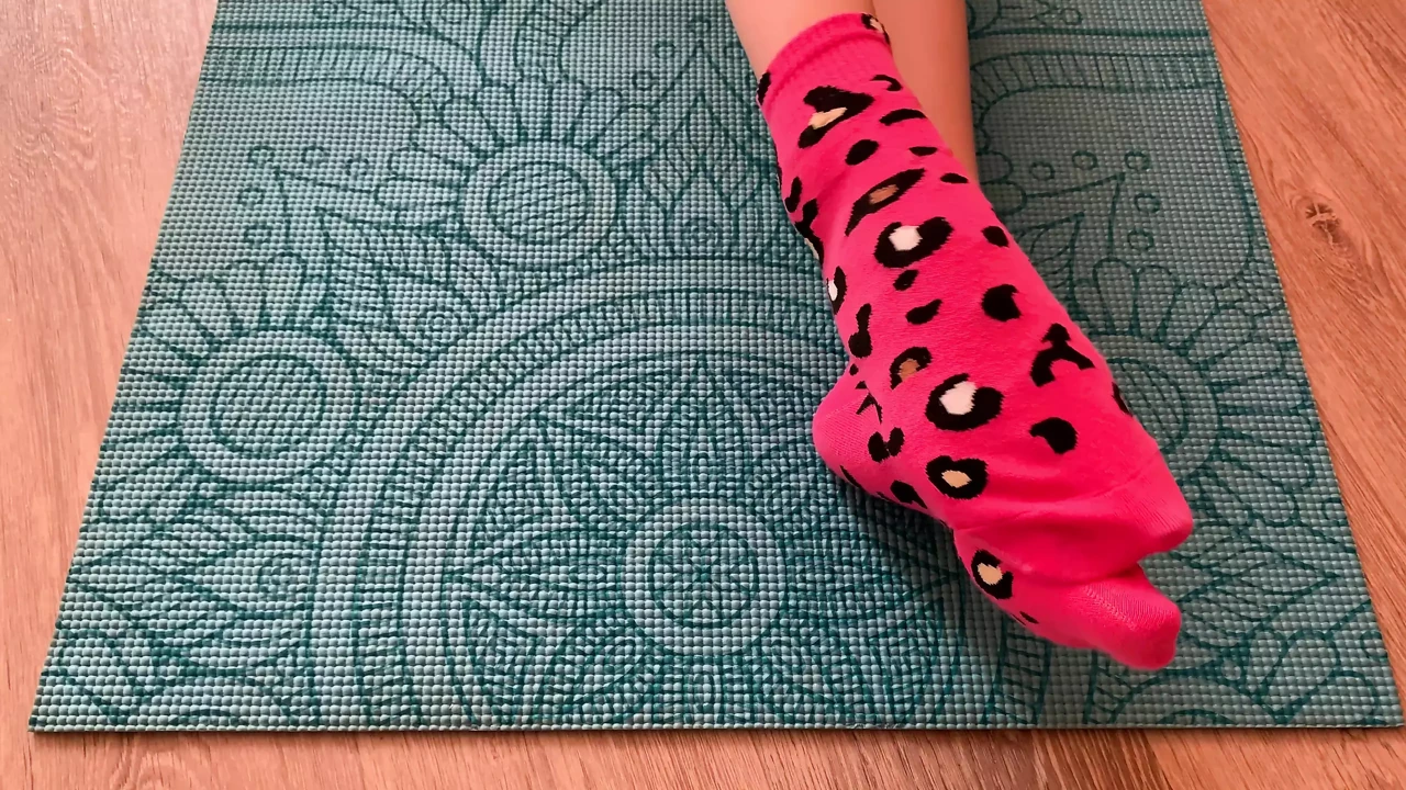 Gloria Gimson in pink socks caresses her feet on a yoga mat