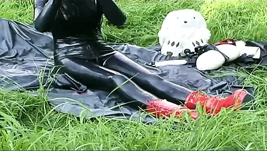 Fetish slave in latex walks and sucks a dildo on the grass
