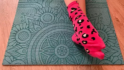 Gloria Gimson in pink socks caresses her feet on a yoga mat