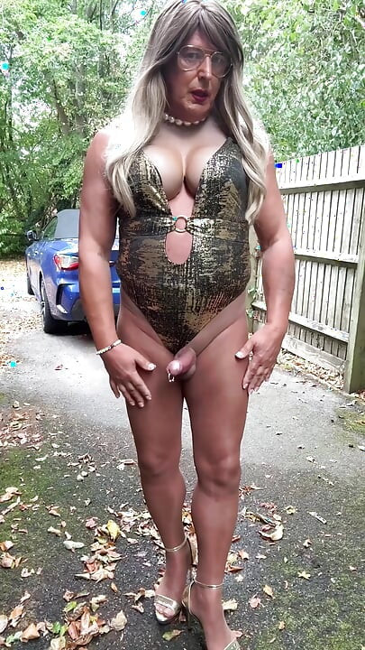 Seksi transvestit kellycd2022 u zlatnom kupaćem kostimu i štiklama čisti lišće