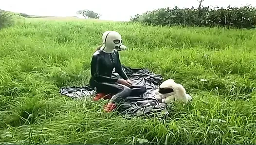 Fetish slave in latex walks and sucks a dildo on the grass
