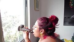 O femeie latino obraznică suge un vibrator cu pulă mare și neagră la fereastră