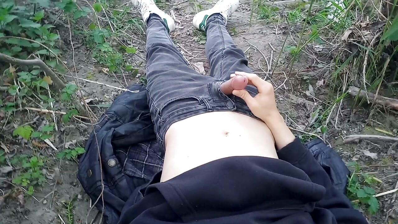 The cute gay twink jerking off his cock, pulled through his fly while outdoors, is Jon Arteen