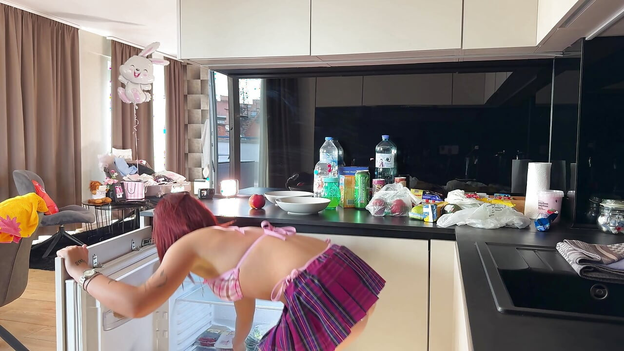 Prawdziwa uczennica w letnim domu przygotowuje kilka owoców w kuchni w najmniejszym bikini z krótką spódnicą
