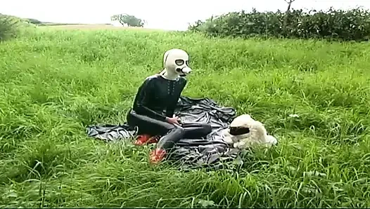 Fetish slave in latex walks and sucks a dildo on the grass