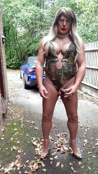 Seksi transvestit kellycd2022 u zlatnom kupaćem kostimu i štiklama čisti lišće