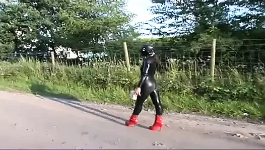 Fetish slave in latex walks and sucks a dildo on the grass