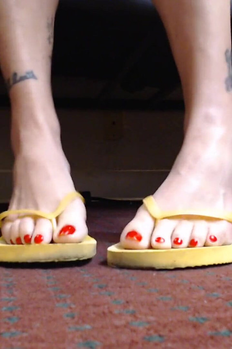 Red toenail wiggling yellow flipflops