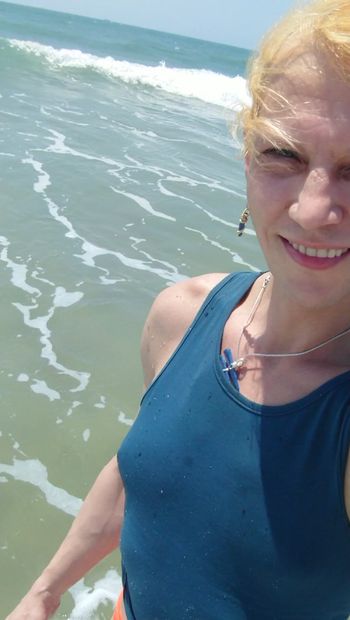 Transgirl nadando en bragas rojas y camiseta azul en el océano Pacífico por primera vez. Disfrutando del sol y el calor. Tetas mojadas en camiseta.