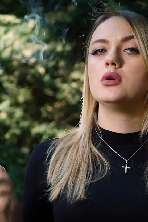 Hete blonde babe die in de natuur een zwarte sigaret rookt