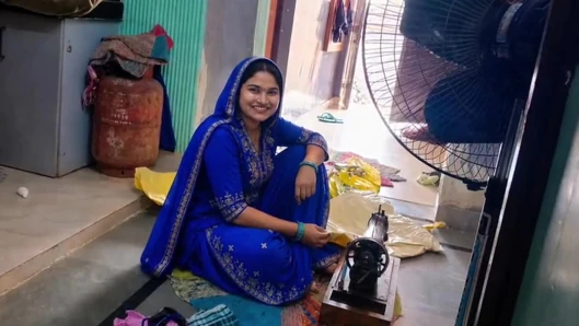 Istri India menjahit pada mesin tetapi dia juga memiliki pemikiran lain.