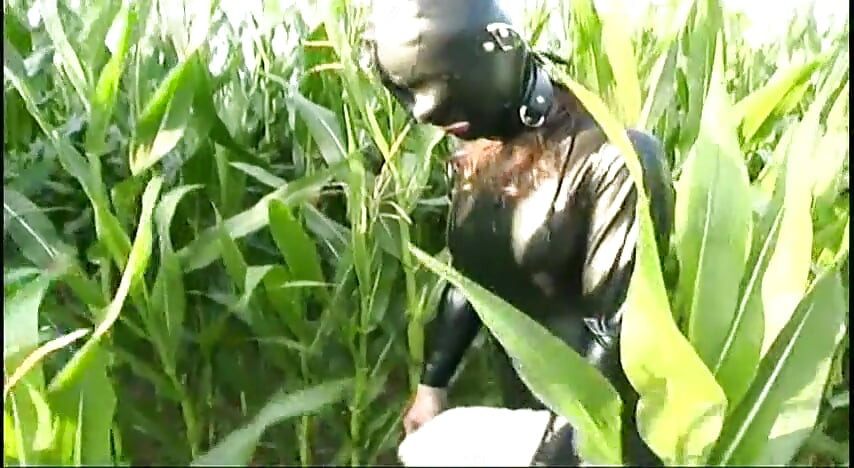 Fetish slave in latex walks and sucks a dildo on the grass