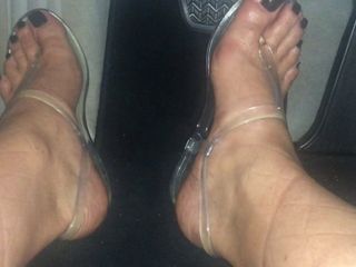 Драйв с обнаженными ступнями и черными ногтями на ногах в прозрачных сандалиях