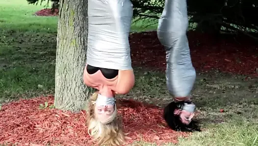 Two girls duct tape mummies outdoors