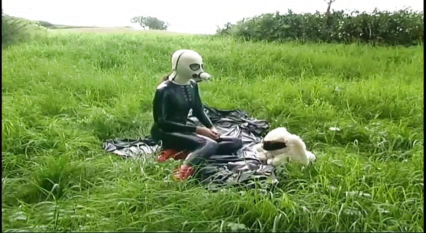 Fetish slave in latex walks and sucks a dildo on the grass