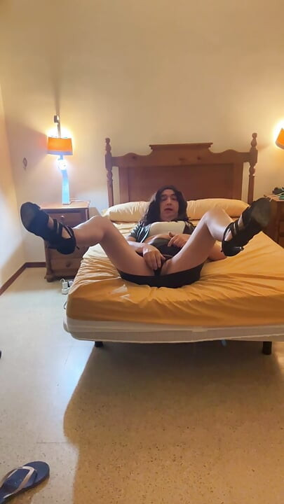 Beautiful and sexy Spanish trans girl masturbates in a tight miniskirt and black latex jacket in the bedroom, wearing high heels