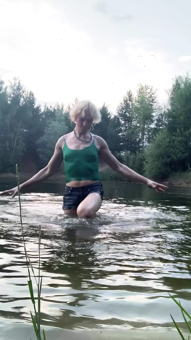Trans girl swimming in the lake in shorts and green top. Wetlook at th lake.