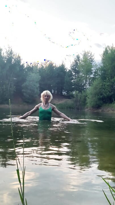 Trans girl swimming in the lake in shorts and green top. Wetlook at th lake.