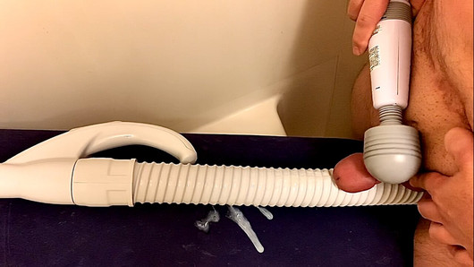 Un vibromasseur à main enfonce un petit pénis sur le tuyau d'un aspirateur et jouit dessus