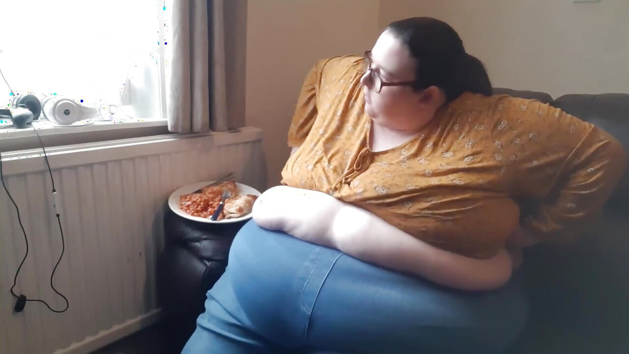 Grandota con enorme barriga mientras come en el sofá