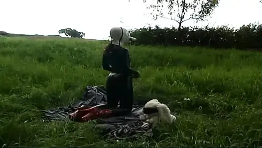 Fetish slave in latex walks and sucks a dildo on the grass