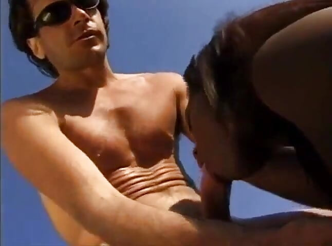 Une chatte poilue noire et blanche baise en position de dogging sur la plage
